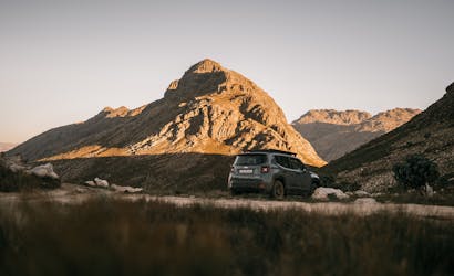A 4x4 vehicle parked on a rugged path amidst scenic mountains under a clear sky.