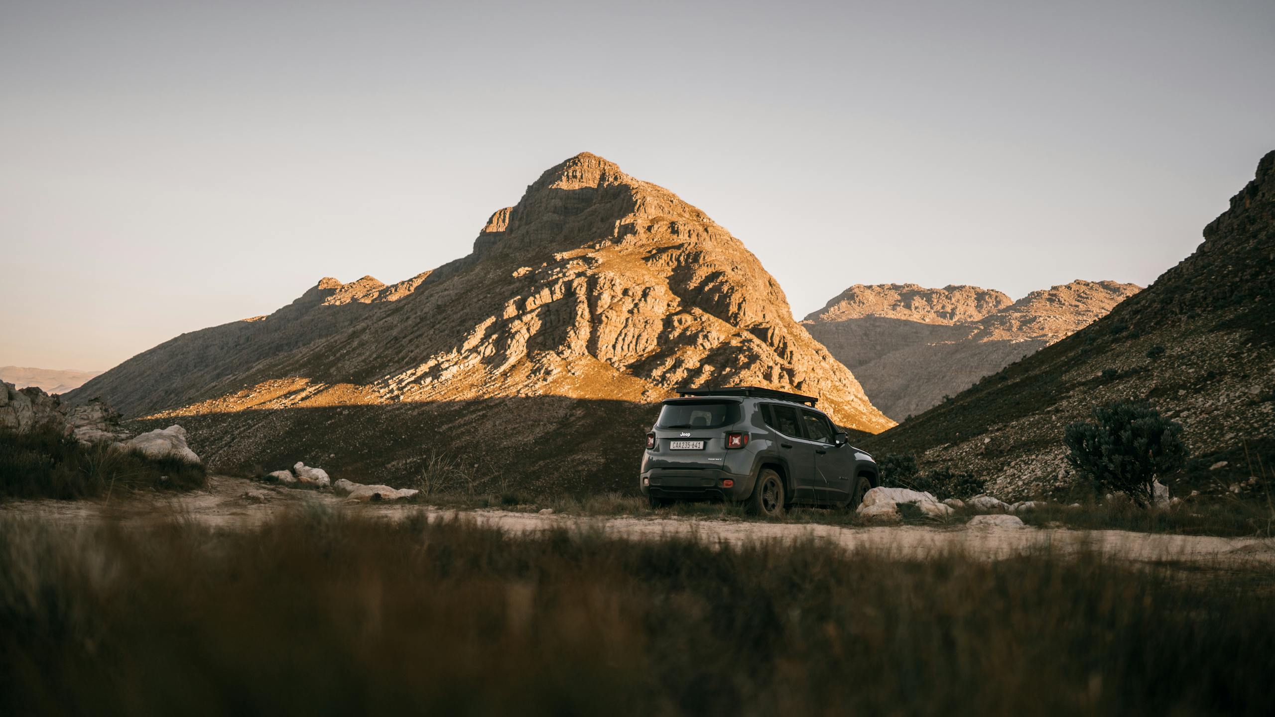 A 4x4 vehicle parked on a rugged path amidst scenic mountains under a clear sky.