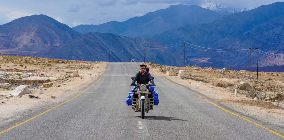 A solitary biker traveling through the rugged terrain of Leh, surrounded by majestic mountains.