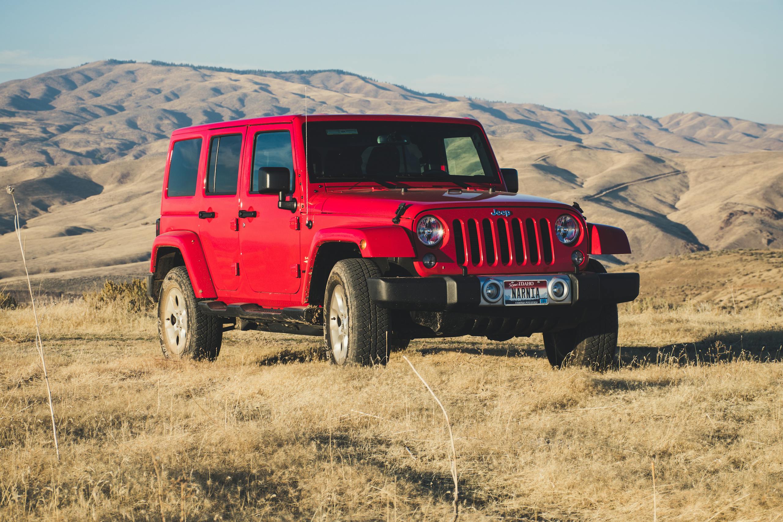A striking red Jeep Wrangler parked in a vast, desert-like landscape under a clear sky.