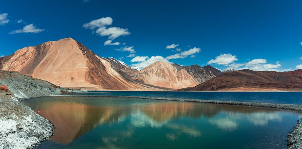 Beautiful panorama of Pangong Lake with majestic Himalayan mountains under a clear blue sky.