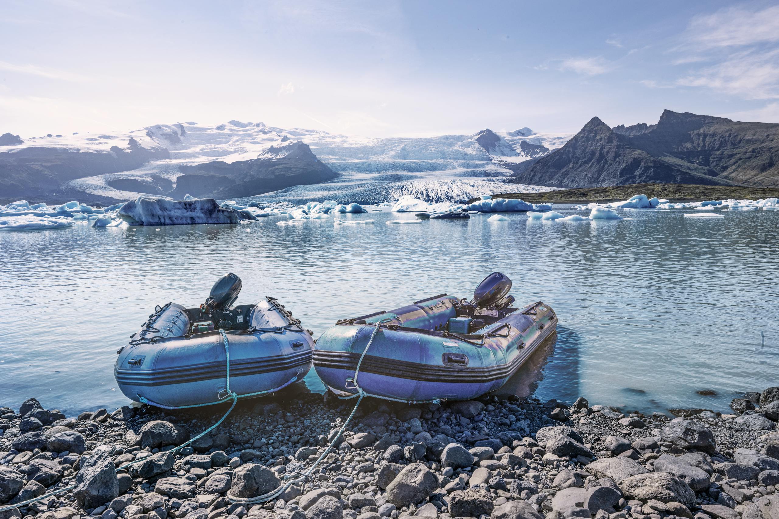 Beautiful view of a glacial lake with inflatable raft boats against majestic Icelandic mountains and icebergs.