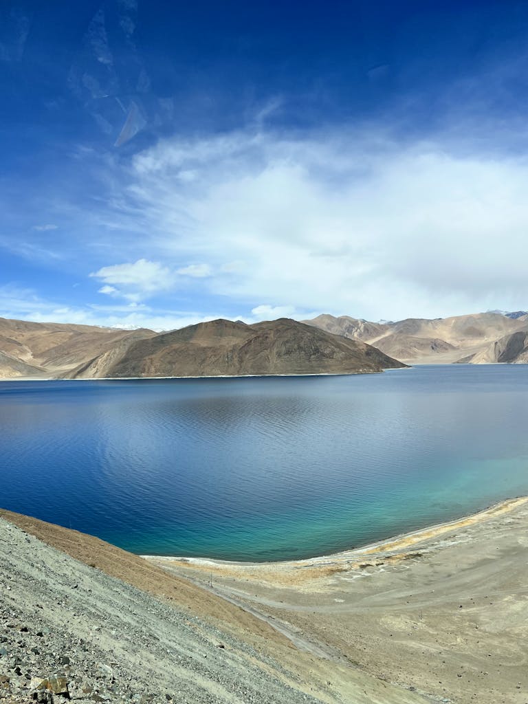 Beautiful view of Pangong Lake surrounded by mountainous terrain under a clear blue sky, capturing nature's serenity.
